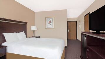 A hotel room with a large bed, a television on a dresser, a nightstand, and a door leading to another room.