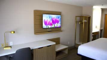 A hotel room with a TV mounted on the wall, a desk with a chair, a bed, and a walk-in closet.