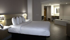 Ett hotellrum med en stor säng, ett nattduksbord med en lampa, ett badrum med badkar och en spegel.