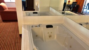 A hotel room with a large bathtub, a sofa, and a mirror reflecting the room. - Econo Lodge Inn & Suites Mckinney - Plano North (McKinney)