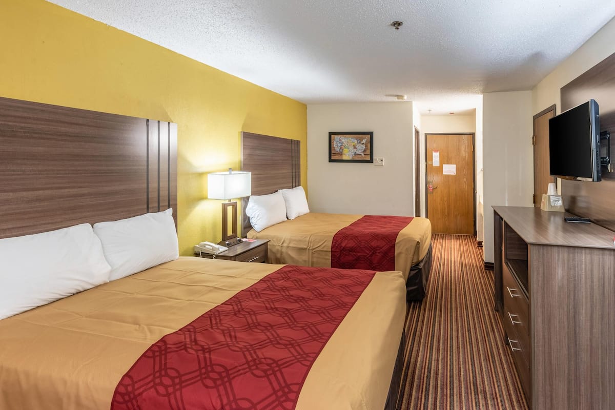 A hotel room with two beds, a desk, a television, and a door.