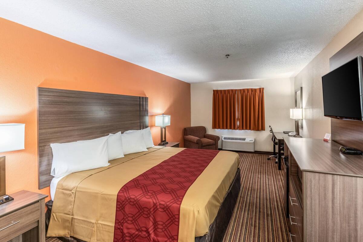 A hotel room with a bed, a desk, a TV, a chair, and a window with curtains.