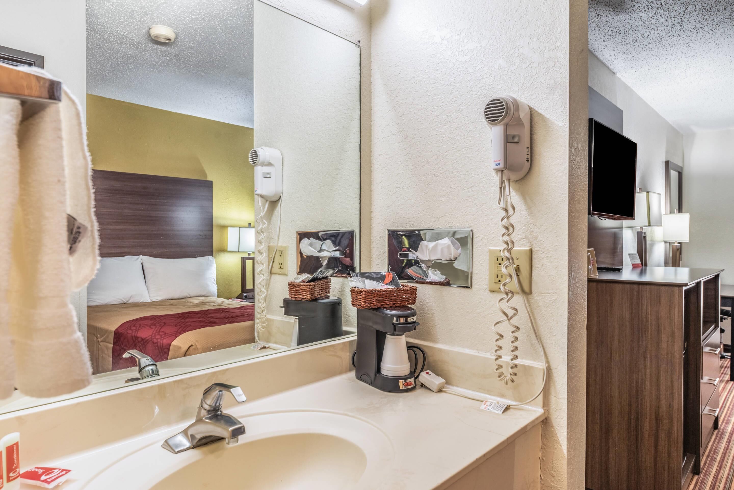 A hotel bathroom with a sink, mirror, hairdryer, and a coffee machine.