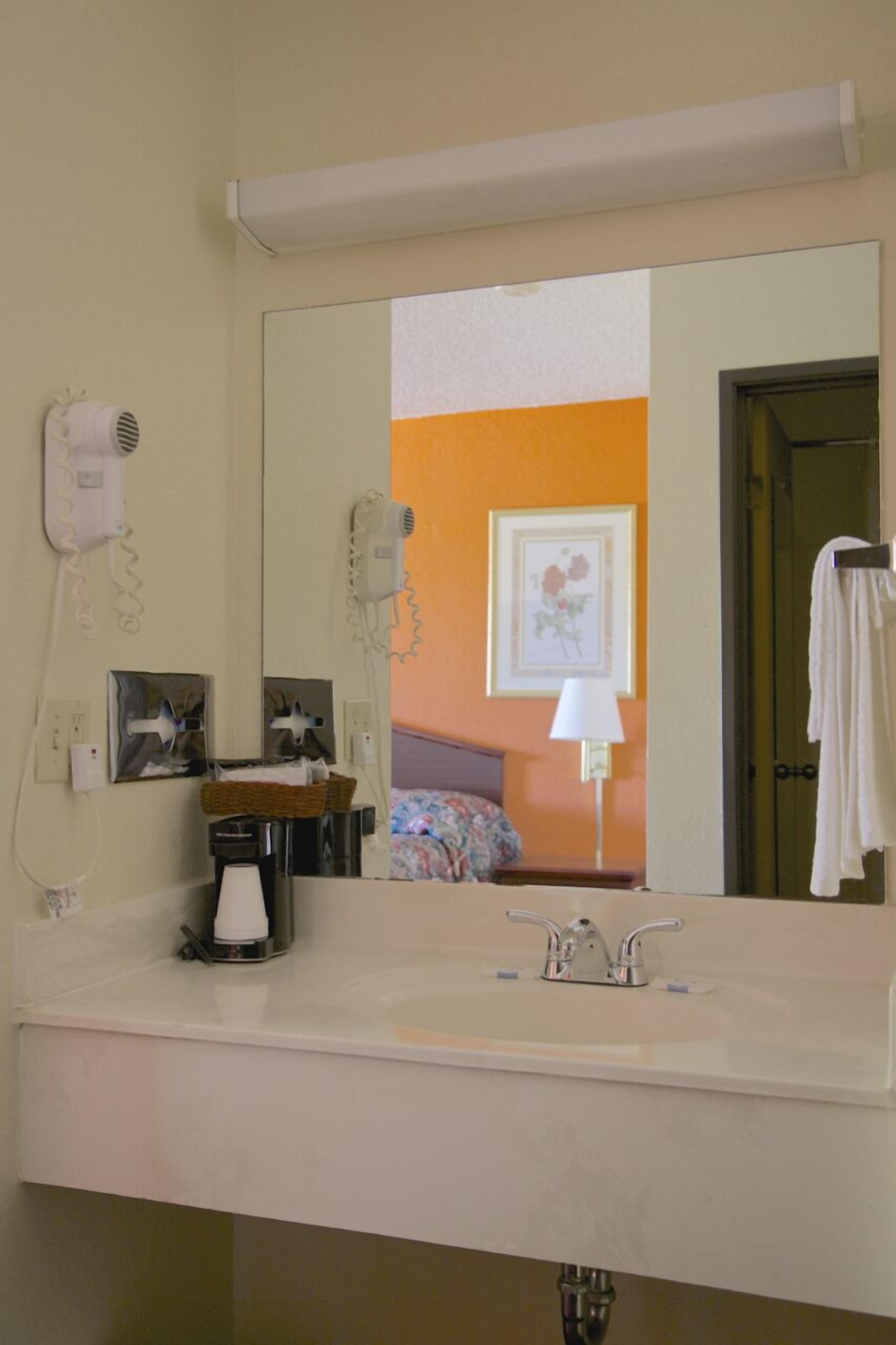 Un baño de hotel con lavamanos, espejo, secador de pelo y toallero.