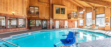 A large indoor swimming pool with wooden walls and a balcony overlooking the pool.