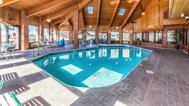 An indoor swimming pool with wooden beams and brick walls, surrounded by lounge chairs and a sunshade. - Econo Lodge Inn & Suites Mckinney - Plano North (McKinney)