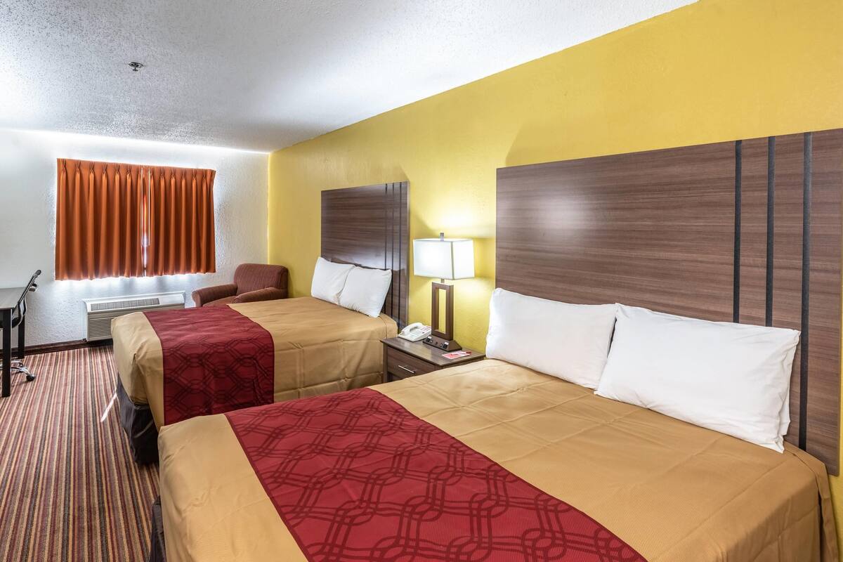 A hotel room with two beds, a desk, a chair, a lamp, and a window with curtains.