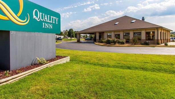 A Quality Inn hotel with a green sign, a parking lot, and a building with a brown roof.