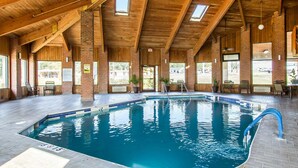 An indoor swimming pool with a wooden ceiling and brick walls, surrounded by seating areas and windows.
