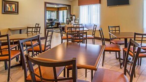 A hotel dining area with multiple tables and chairs, a television mounted on the wall, and a view of the lobby through a glass door. - Quality Inn Murray University Area (Murray)