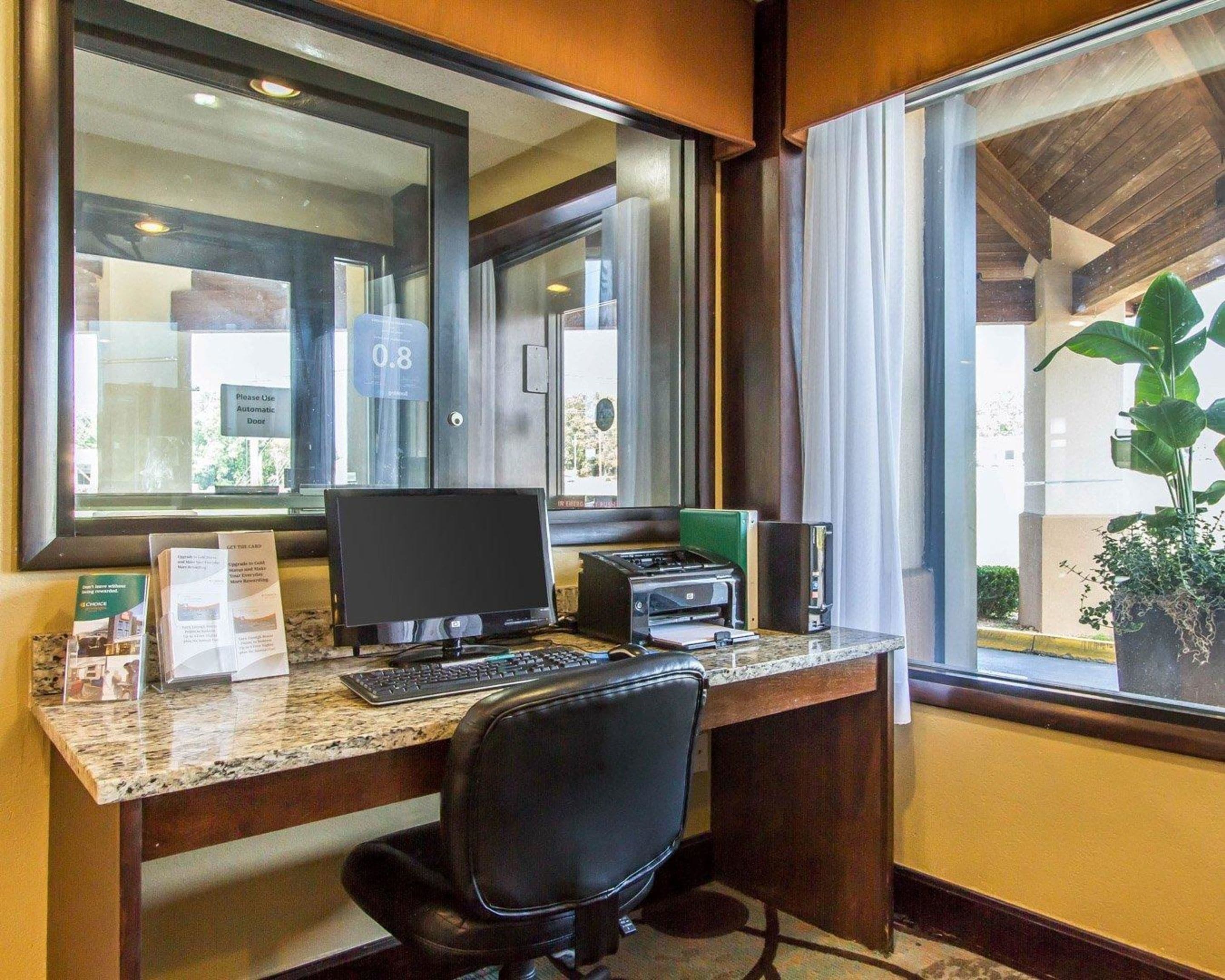 A hotel room with a desk, computer, printer, and a window with a view of the outdoors.