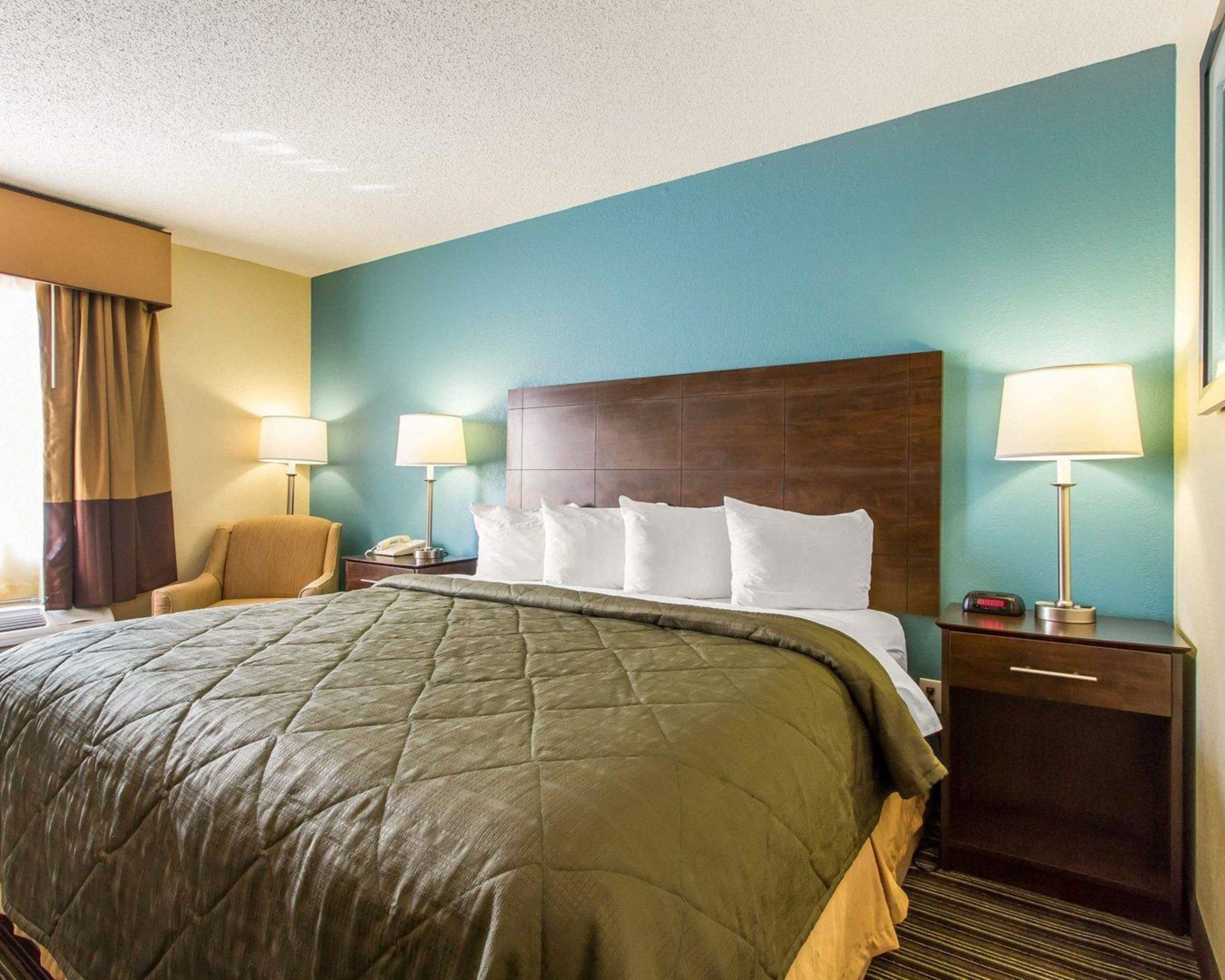 A hotel room with a large bed, two bedside tables with lamps, a chair, and a nightstand with a phone.
