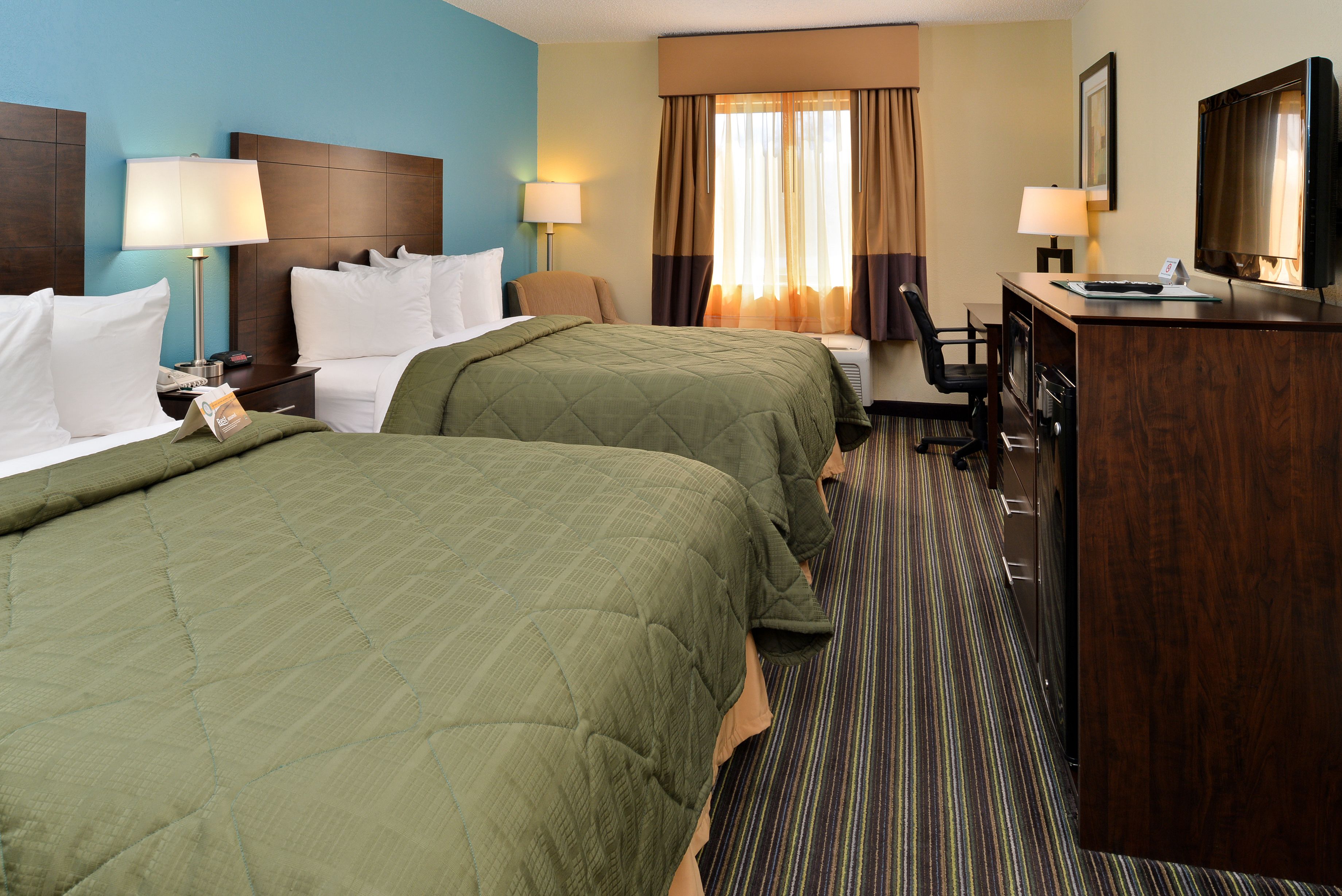 A hotel room with two beds, a desk, a chair, a television, and a window with curtains.