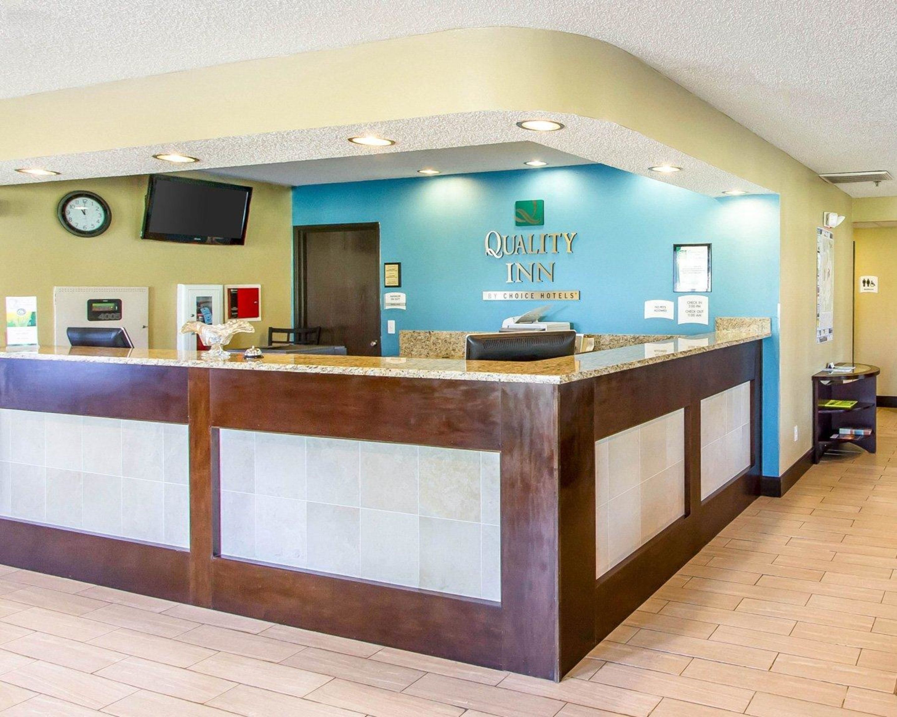 A reception desk with a clock, a television, and a sign for Quality Inn by Choice Hotels.