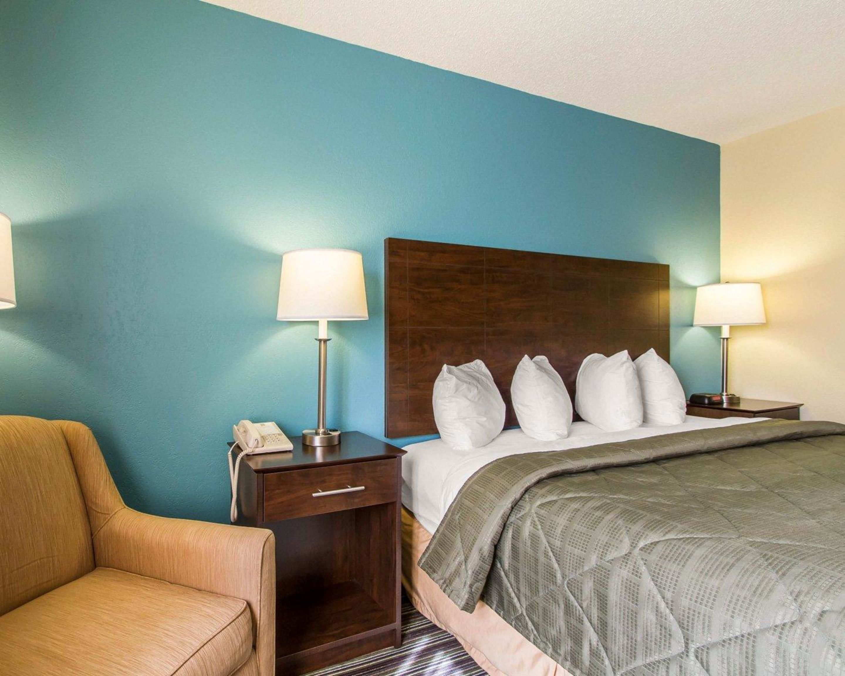 Une chambre d’hôtel avec un grand lit, deux tables de chevet avec des lampes, une chaise et un téléphone situé du côté gauche.