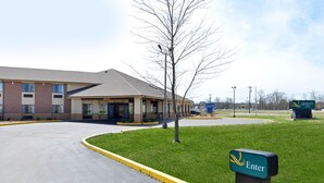 A hotel entrance with a green lawn, a sign indicating the entrance, and a building with multiple windows and a flat roof.