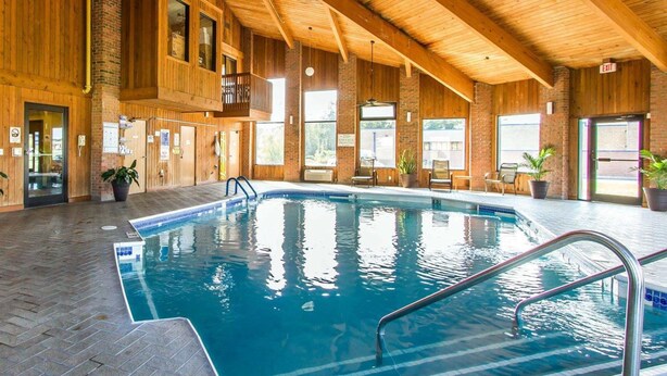 An indoor swimming pool with wooden beams, a tiled floor, and a view of the outside through large windows. - Quality Inn Murray University Area (Murray)
