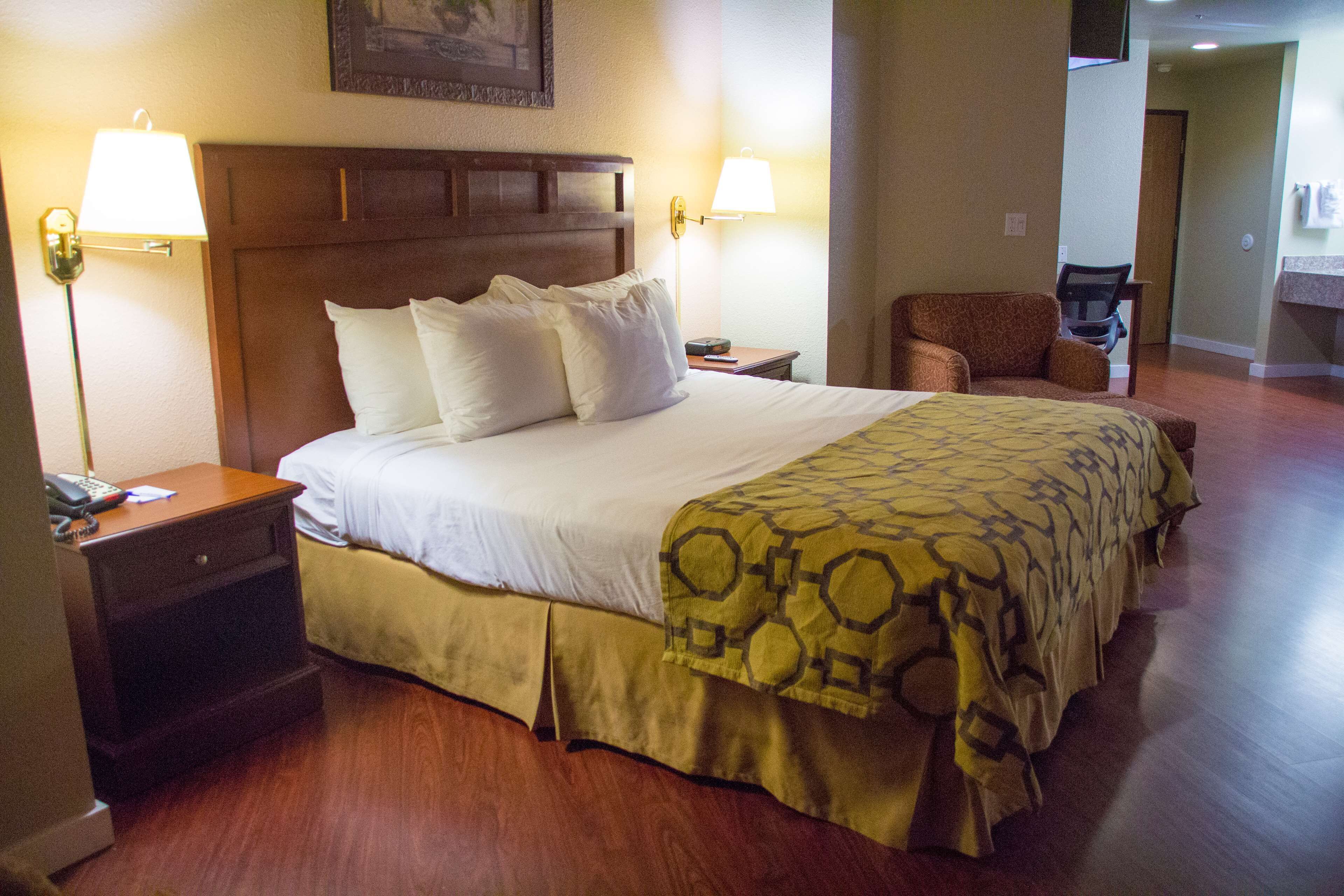 A hotel room with a large bed, two bedside lamps, a wooden headboard, a nightstand with a telephone, and a chair.