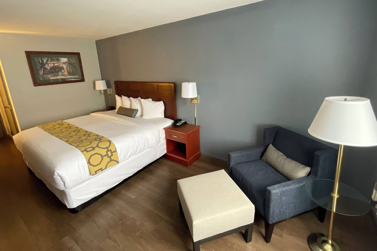 Una habitación de hotel con una cama grande, una mesita de noche con una lámpara, una silla y una pequeña mesa.