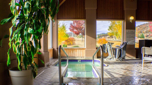 Zona de piscina con vista a follaje otoñal, planta en maceta y cartel con normas del spa.