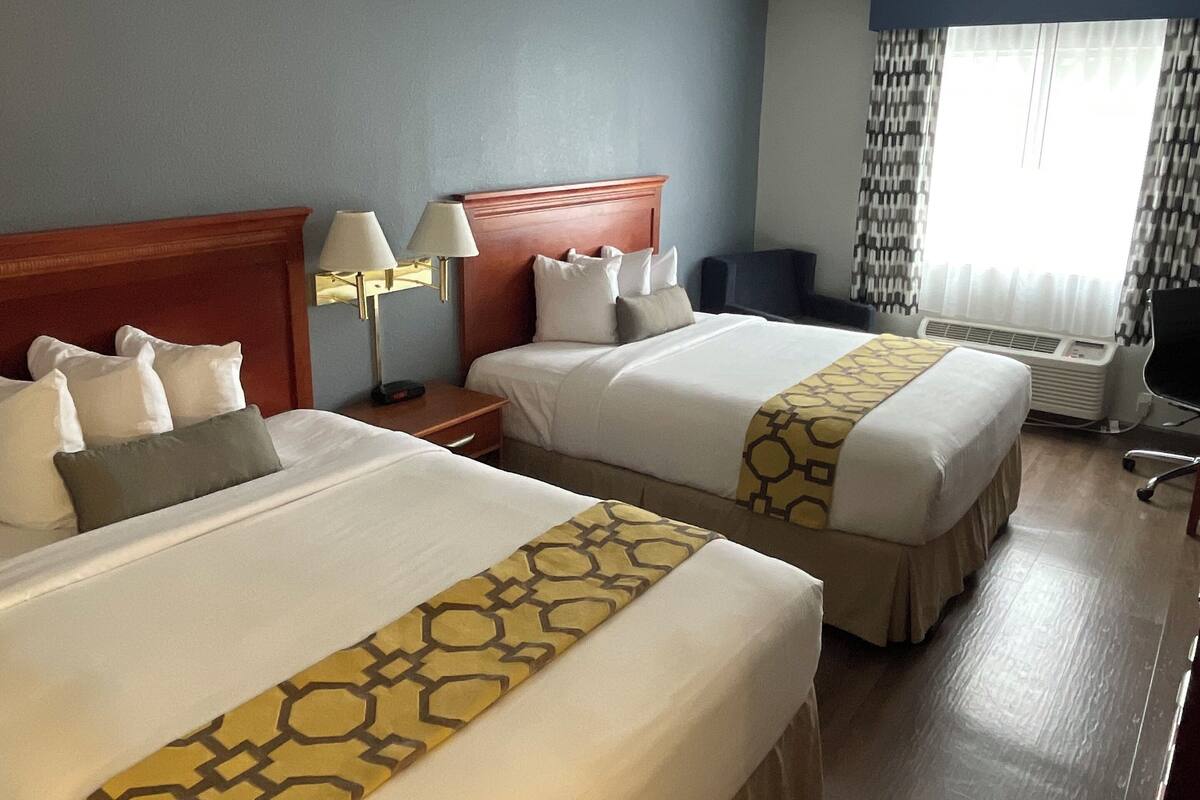 Una habitación de hotel con dos camas, un escritorio, una silla, una lámpara y una ventana con cortinas.