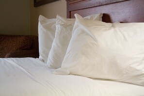 Een net opgemaakt bed met wit beddengoed en kussens, een houten hoofdeinde, en een bruine gestreepte bank op de achtergrond.