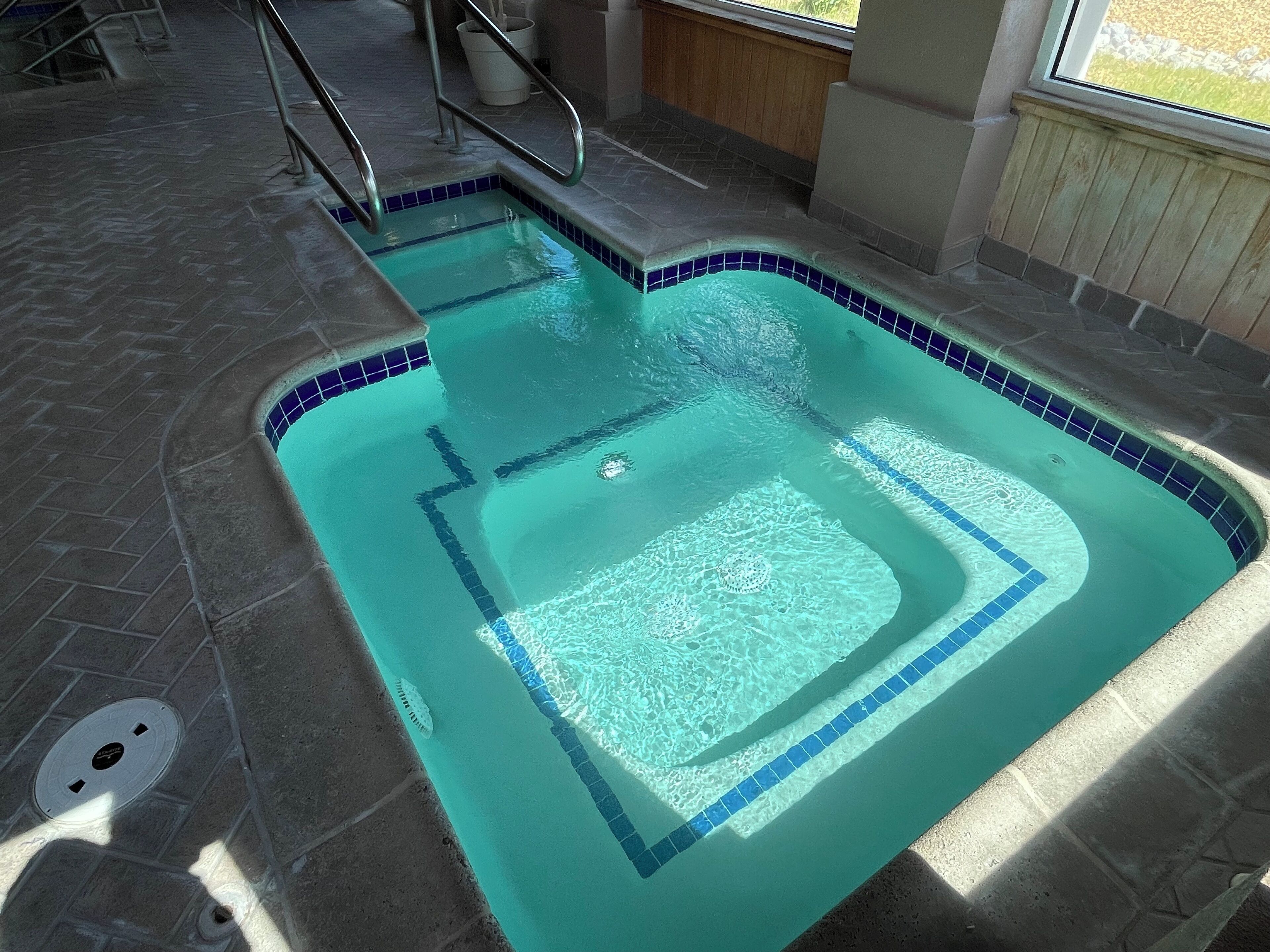 A rectangular indoor pool with clear blue water, tiled edges, and a metal ladder leading into the pool.