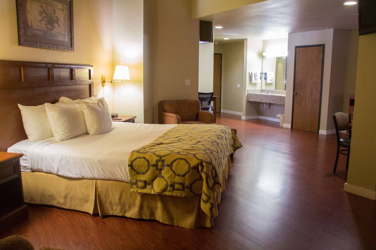 Habitación de hotel con una cama grande, una silla, un escritorio y un baño visible a través de una puerta abierta.
