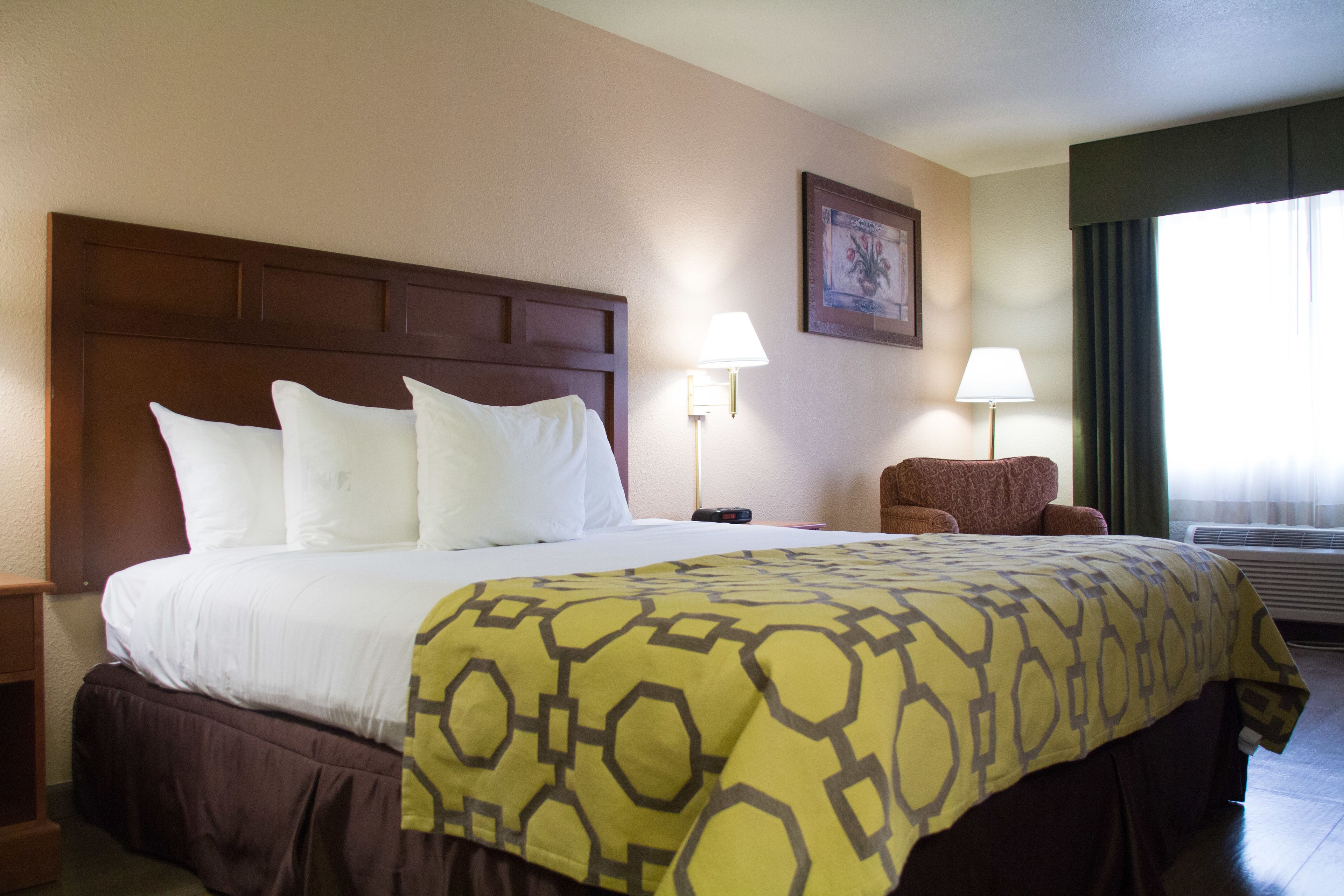 A hotel room with a large bed, two bedside lamps, a chair, and a window with curtains.