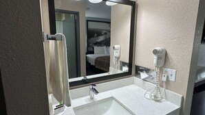 A hotel bathroom with a large mirror, a sink, a hairdryer, and a towel rack.