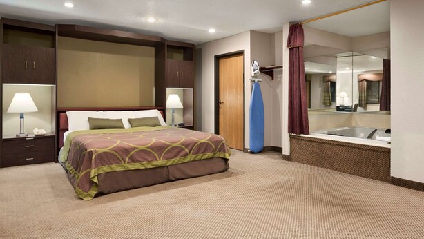 A hotel room with a bed, two bedside tables with lamps, a large mirror, and a bathroom with a bathtub.