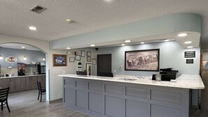 A modern reception area with a marble counter, framed pictures on the wall, and a kitchen in the background.