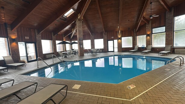 An indoor swimming pool with a brick floor, lounge chairs, and tables. - SureStay by Best Western Grove City (Grove City)