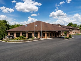 A hotel with a brick facade, a covered parking area, and a landscaped front yard.
