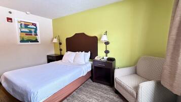 A hotel room with a bed, a chair, a nightstand, and a wall-mounted lamp.