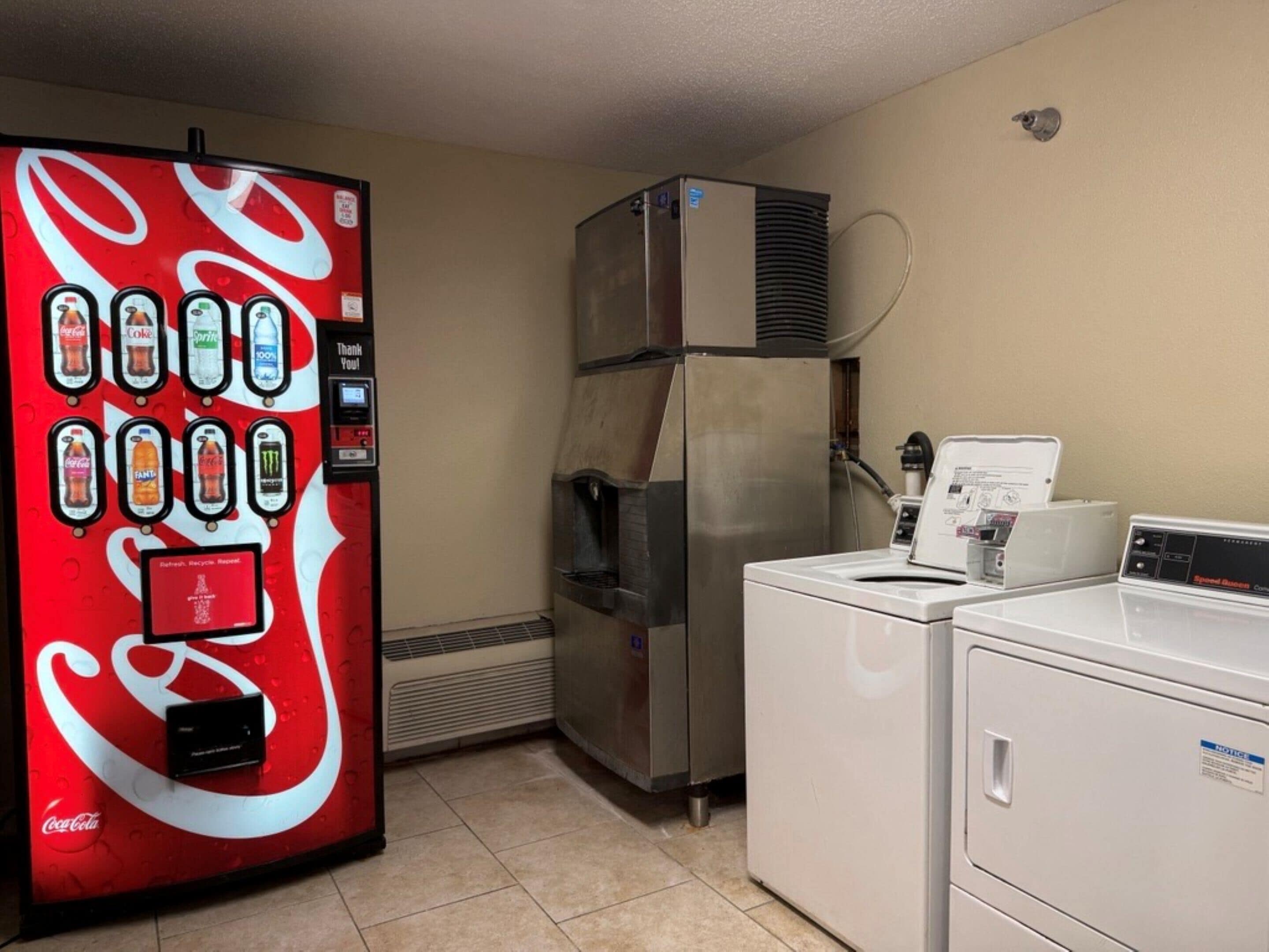 Una kitchenette con una máquina expendedora de refrescos, un refrigerador y una lavadora.