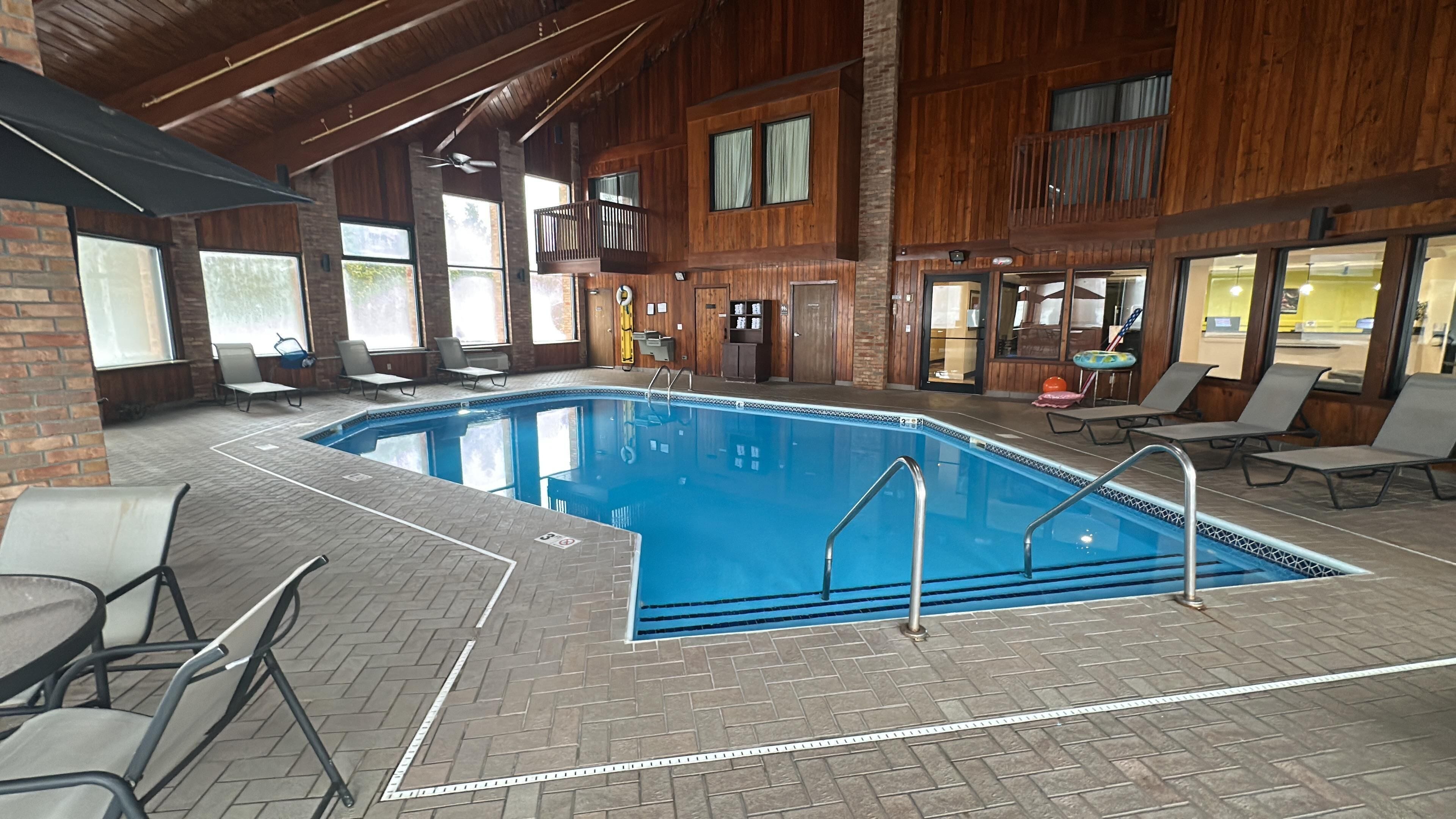 Una piscina interior con suelo de ladrillo y sillones de descanso alrededor.