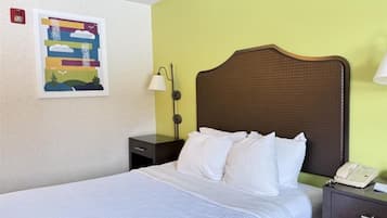 A hotel room with a bed, a nightstand with a lamp, a phone, and a wall-mounted picture.