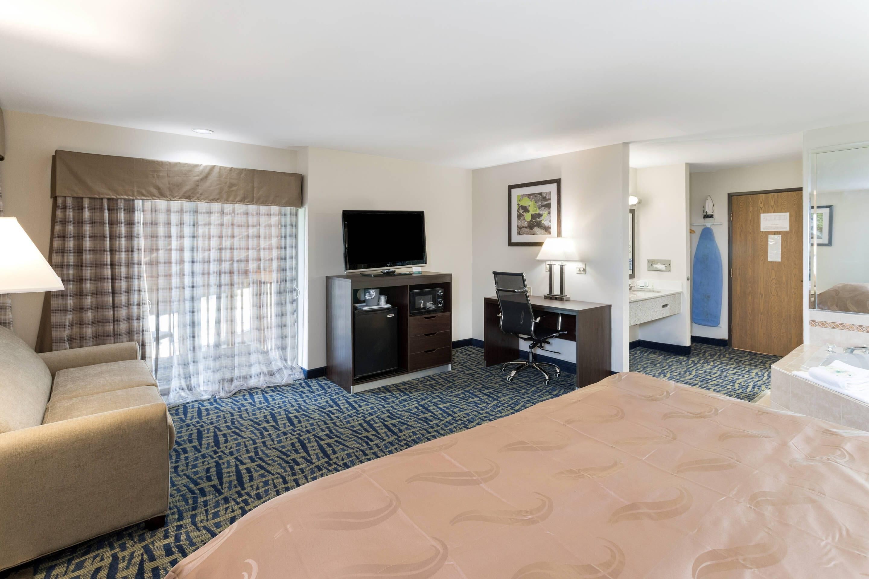 Une chambre d’hôtel comprenant un lit, un bureau, une télévision, une chaise et une salle de bain.