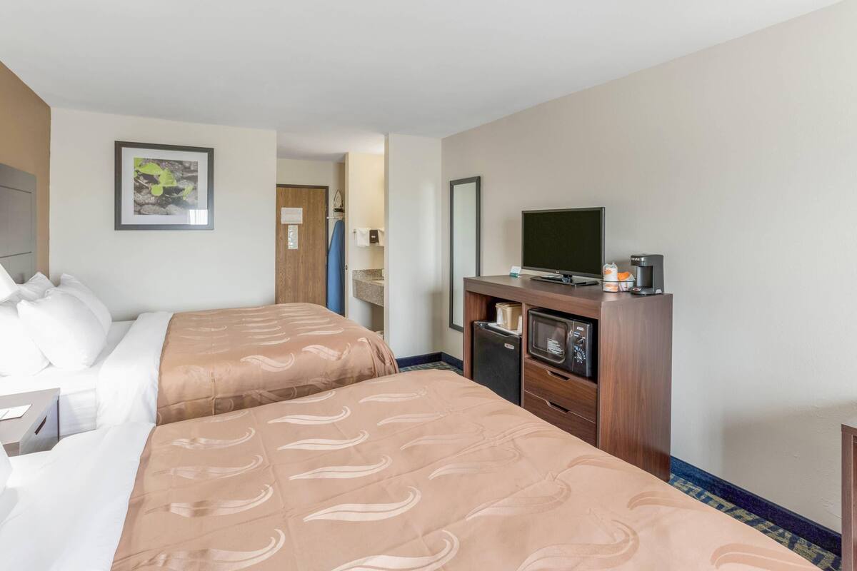 Una habitación de hotel con dos camas, televisión, cafetera y un escritorio pequeño.