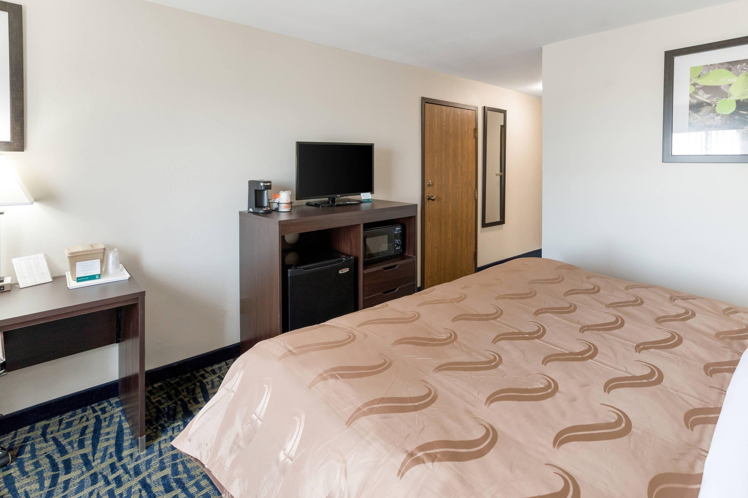 Una habitación de hotel con una cama, un escritorio con televisor, una cafetera y un minibar.