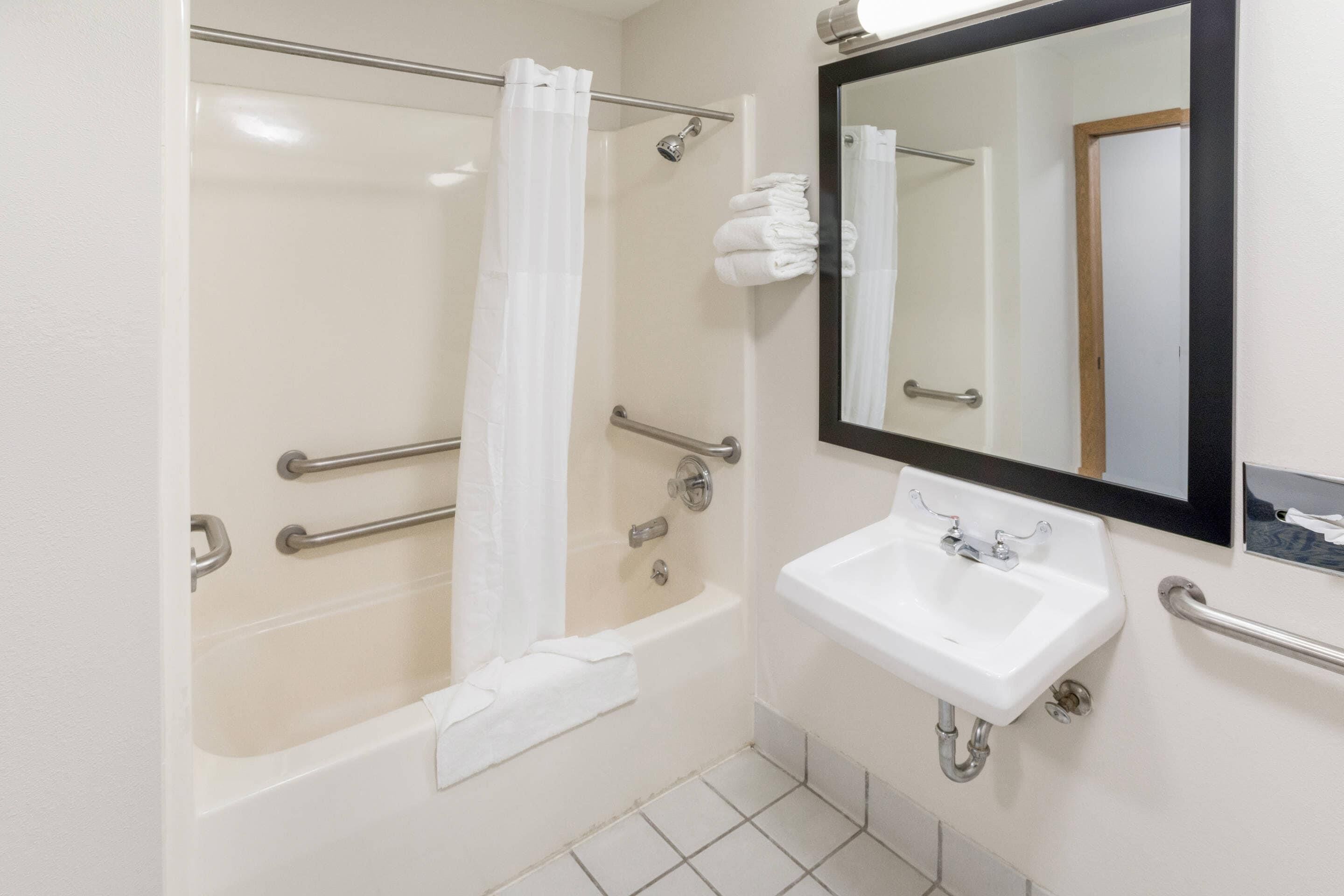 Un baño con bañera, lavamanos, espejo y barras de apoyo.
