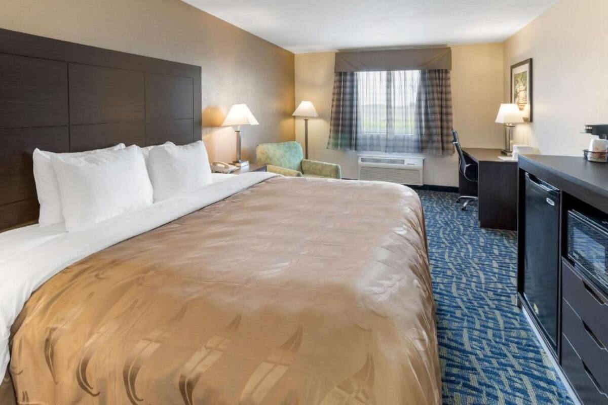 Habitación de hotel con una cama grande, dos lámparas de noche, un escritorio con silla y un ventanal con cortinas.