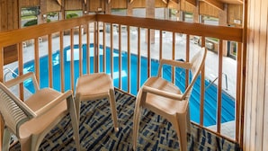 A pool area with wooden railings, three plastic chairs, and a patterned floor.