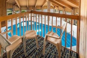 Zona de piscina con barandillas de madera, tres sillas de plástico y suelo estampado.