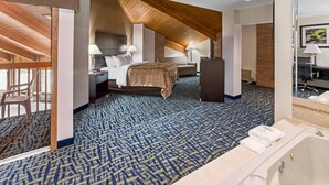 A hotel room with a large bed, two bedside tables, a desk, a chair, a bathroom with a bathtub, and a patterned carpet.