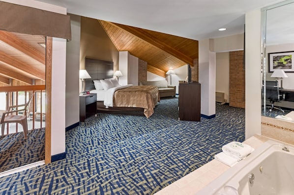 A hotel room with a large bed, two bedside tables, a desk, a chair, a bathroom with a bathtub, and a patterned carpet.