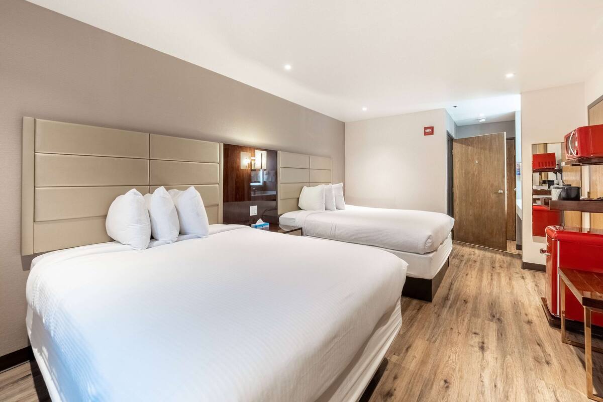 A hotel room with two beds, a wooden floor, a red cabinet, and a door leading to another room.