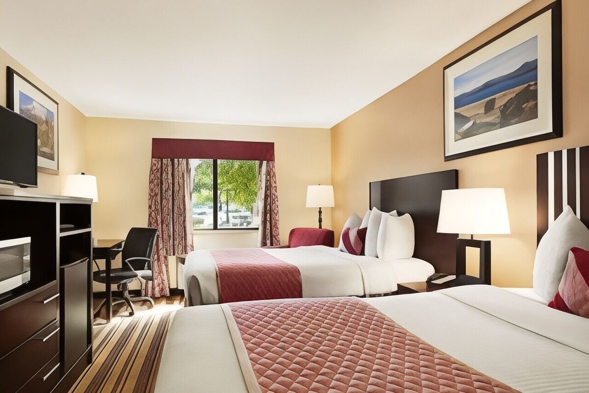 Une chambre d’hôtel avec deux lits, un bureau, une télévision et une fenêtre avec des rideaux.