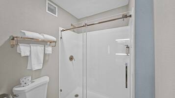 A bathroom with a glass-enclosed shower, a toilet, and a towel rack with towels.